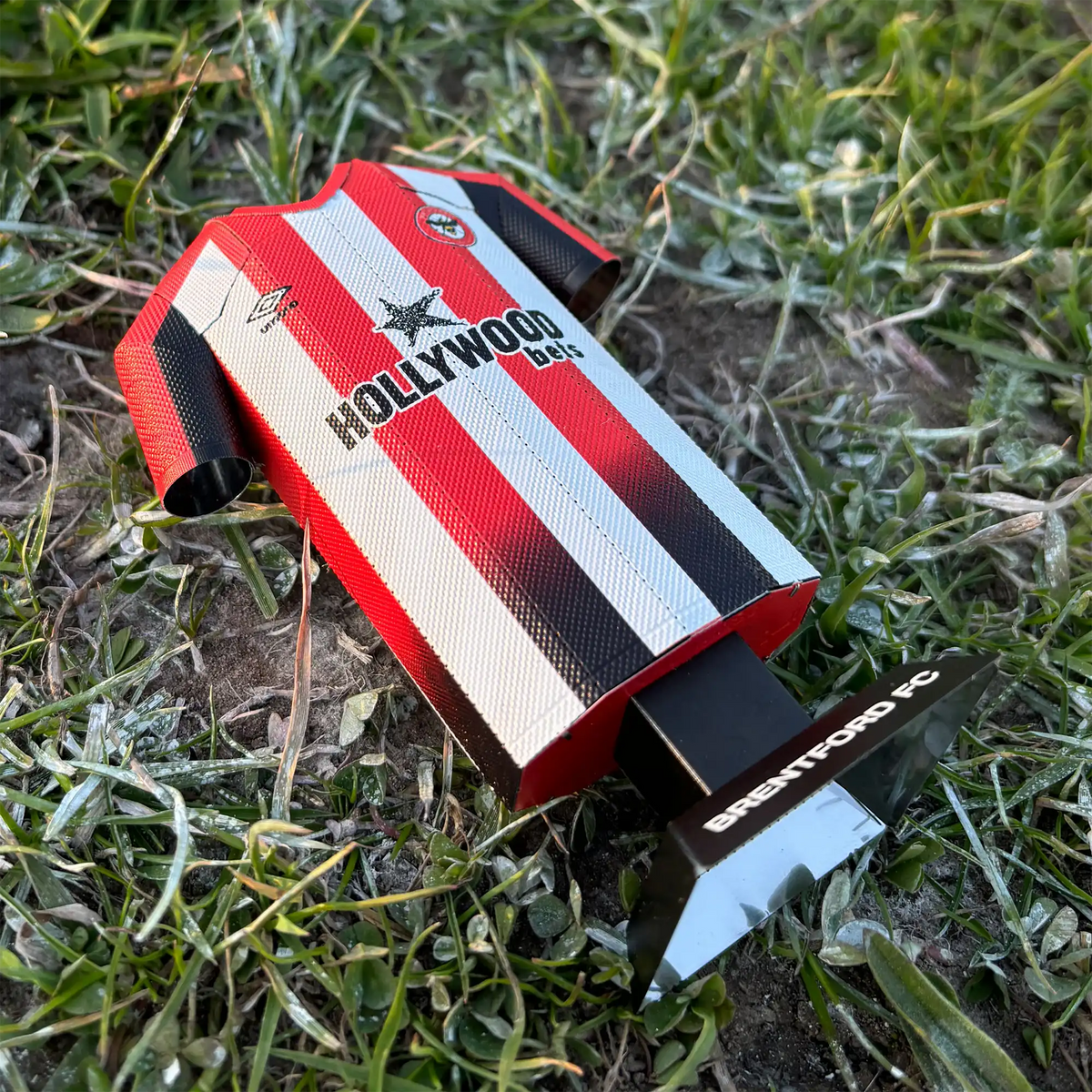 Square lifestyle product photograph showcasing the Brentford FC 2024/2025 traditional red and white striped home jersey collectible styled in a real-world setting.