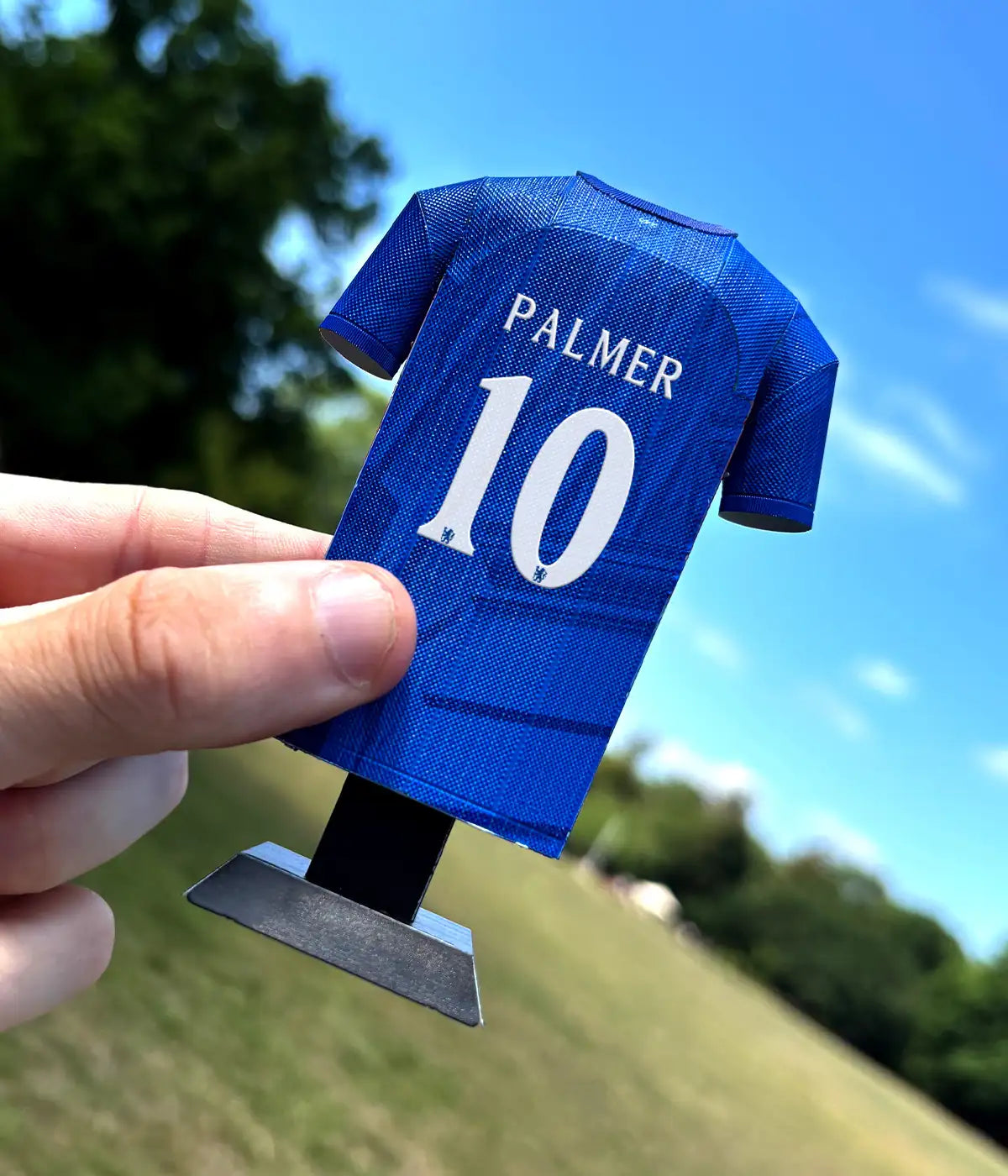 Blue sports jersey with 'PALMER 10' printed on it held against a blurred outdoor background.