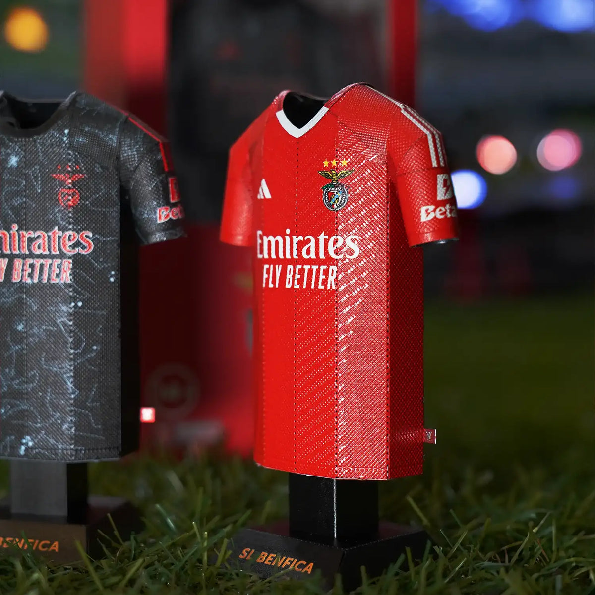 Lifestyle product photograph showcasing SL Benfica 2024/2025 red home jersey collectibles styled on an outdoor grass turf.