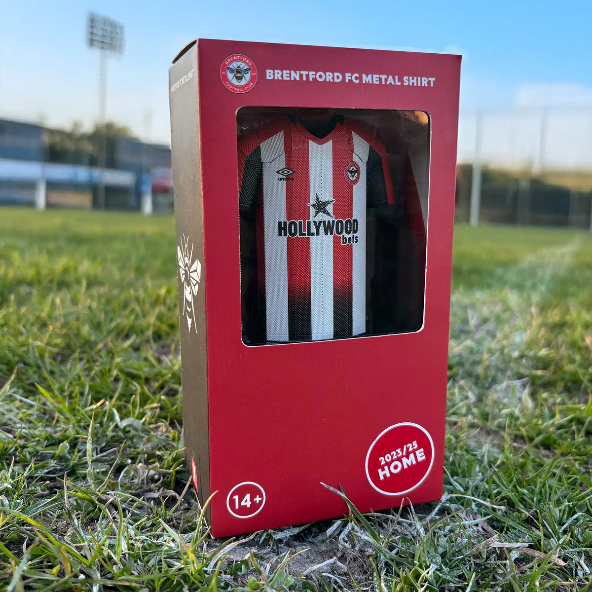 Square lifestyle product photograph showcasing the Brentford FC premium display case standing upright on grass.