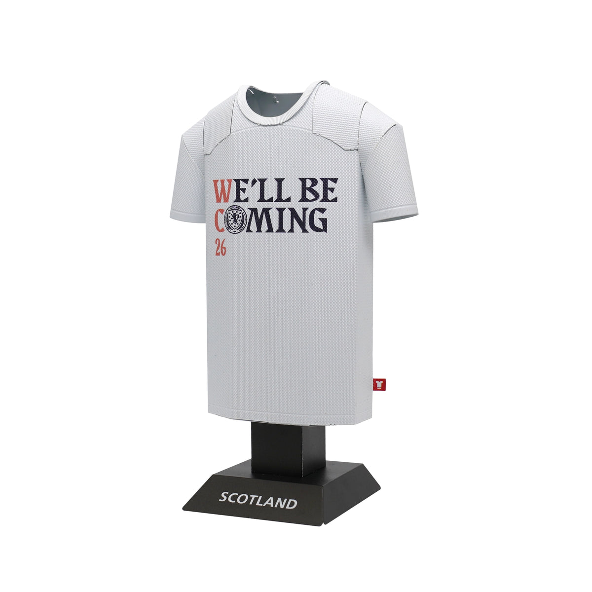 White sports jersey with 'We'll Be Coming' text on a black stand with 'Scotland' label