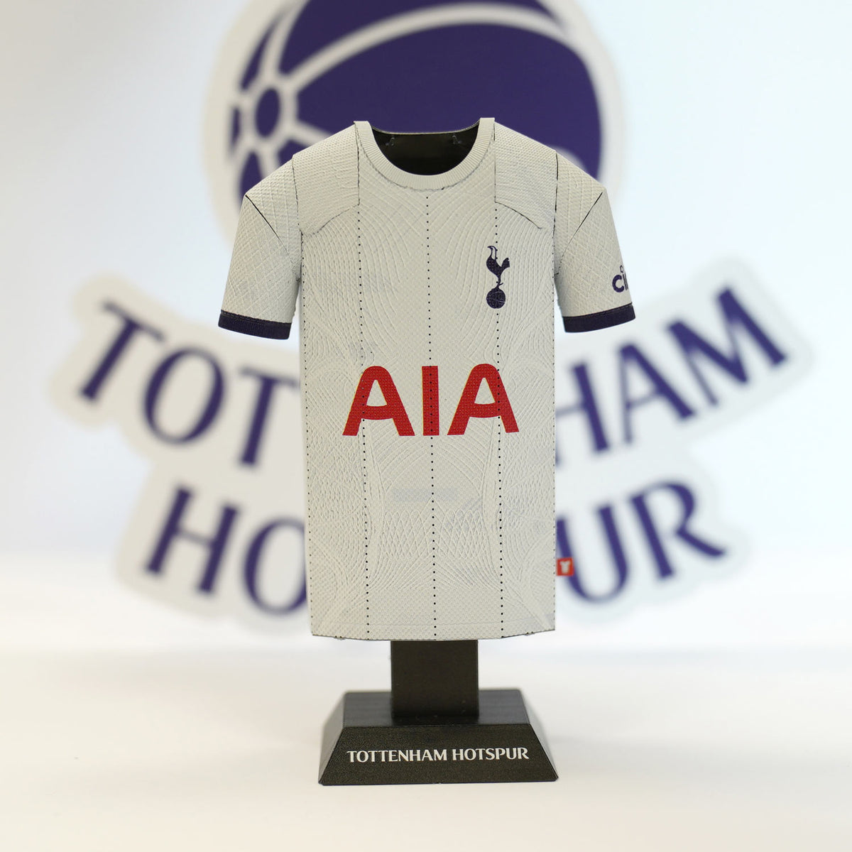 A detailed close-up focusing on the collar line and official team emblem of the white Tottenham Hotspur 2023/2024 home miniature jersey collectible